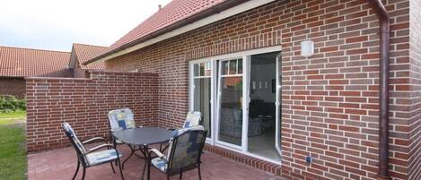 Un patio con una mesa, sillas, un muro de ladrillo y una puerta corrediza de vidrio.