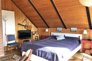 Ein Schlafzimmer mit einem Bett, einem Fernseher, einer Gitarre und einer Holzbalkendecke.