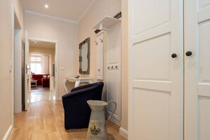 A hallway with a dark blue armchair, a white door, and a vintage-style vase with 'MAJESTIC' written on it. - No. 9 in Villa Aegir (Ostseebad Binz)