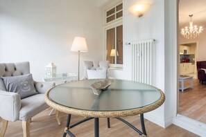 A room with a round glass table, a sofa with cushions, a lamp, and a view into a kitchen area. - No. 9 in Villa Aegir (Ostseebad Binz)