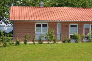 A single-story brick house with a red-tiled roof, a small front porch, and a view of a body of water with a sailboat. - Holiday home in Kosel with swimming pool (Kosel)