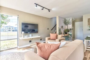Ein modernes Wohnzimmer mit Flachbildfernseher, einer Couch, einem Couchtisch und einer Treppe, die eine weitere Ebene hinaufführt.
