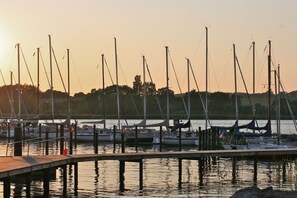 Ein Yachthafen mit mehreren dort liegenden Booten, eine Holzstege und ruhiges Gewässer, das den Himmel spiegelt.