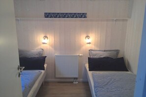 Een kamer met twee bedden, elk voorzien van gestreept beddengoed, een witte radiator en wandlampen.