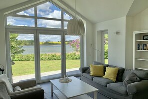 A living room with a large window, a grey sofa, a white coffee table, and a bookshelf. - Holiday home in Kosel with swimming pool (Kosel)