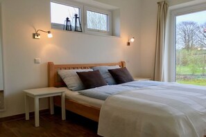 Ein Schlafzimmer mit einem Bett, einem Nachttisch, zwei Wandleuchten, einem Fenster und Blick auf Grünfläche.