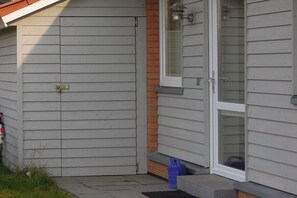 Ein Haus mit einer geschlossenen, grauen Tür, einem Fenster mit einer Scheibe und einem blauen Gegenstand auf der Stufe.