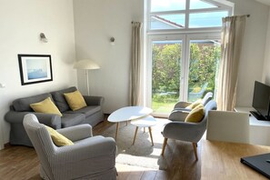 Ein modernes Wohnzimmer mit einem grauen Sofa, einem karierten Sessel, einem weißen Couchtisch und einem Fernseher auf einem Schrank.