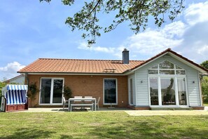 Ein zweistöckiges Haus mit einem Ziegeldach, einer überdachten Veranda mit Tisch und Stühlen und einem großen Schiebeglasfenster.