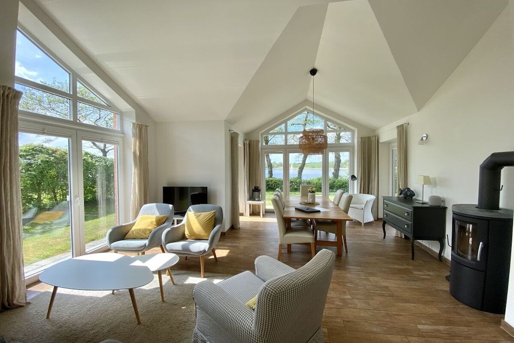 A spacious living area with a large dining table, comfortable seating, a fireplace, and large windows offering a view of the outdoors.