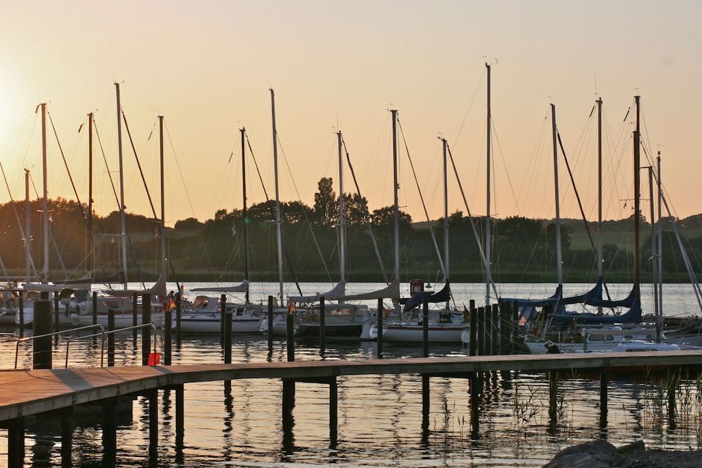A marina with multiple boats docked, a wooden pier, and a calm water body reflecting the sky.