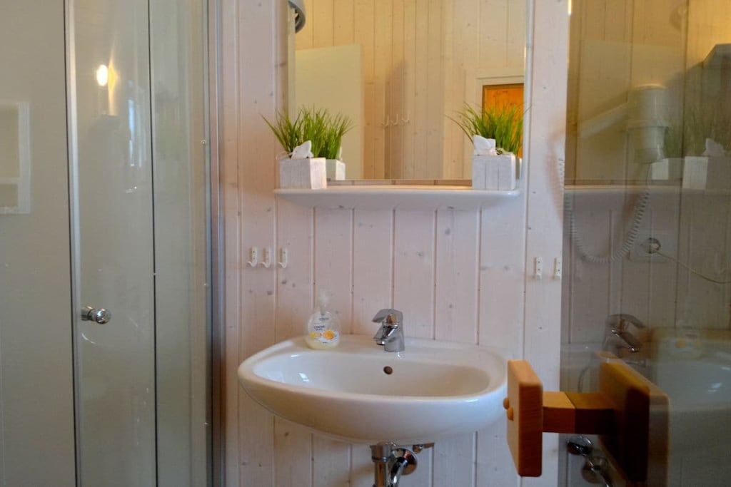 Un baño con un lavabo blanco, un espejo encima y dos plantas en macetas sobre una repisa.