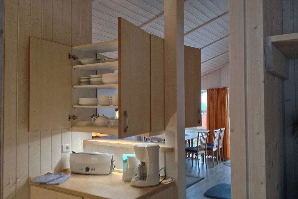 A compact kitchen with a coffee maker, a toaster, and a shelf with dishes.