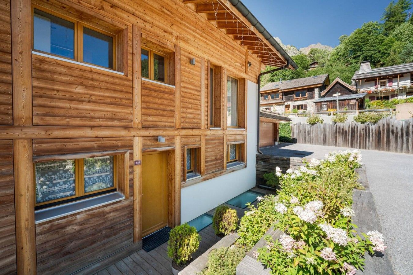A wooden chalet with a wooden deck, a small garden, and a mountain backdrop.