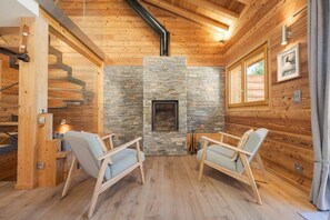 A cozy cabin interior with a stone fireplace, wooden walls, and two light-colored chairs. - 145-square-meter Chalet | View | Quiet | Sauna | Jacuzzi (Chamonix-Mont-Blanc)
