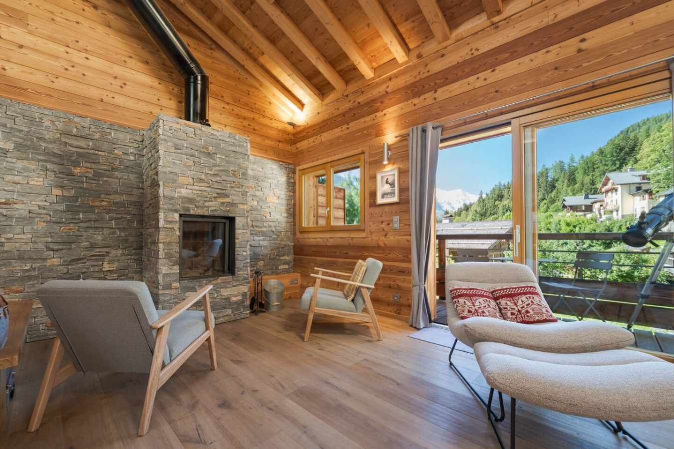 A cozy cabin interior with a stone fireplace, wooden walls, and a balcony with a view of the mountains.