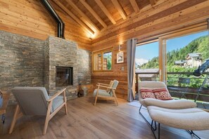 A cozy cabin interior with a stone fireplace, wooden walls, and a balcony with a view of the mountains. - 145-square-meter Chalet | View | Quiet | Sauna | Jacuzzi (Chamonix-Mont-Blanc)
