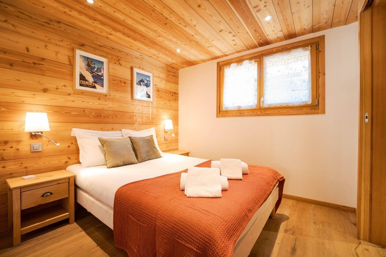 Ein Zimmer mit Holzwänden, einem Bett, Nachttischen und Wandlampen.