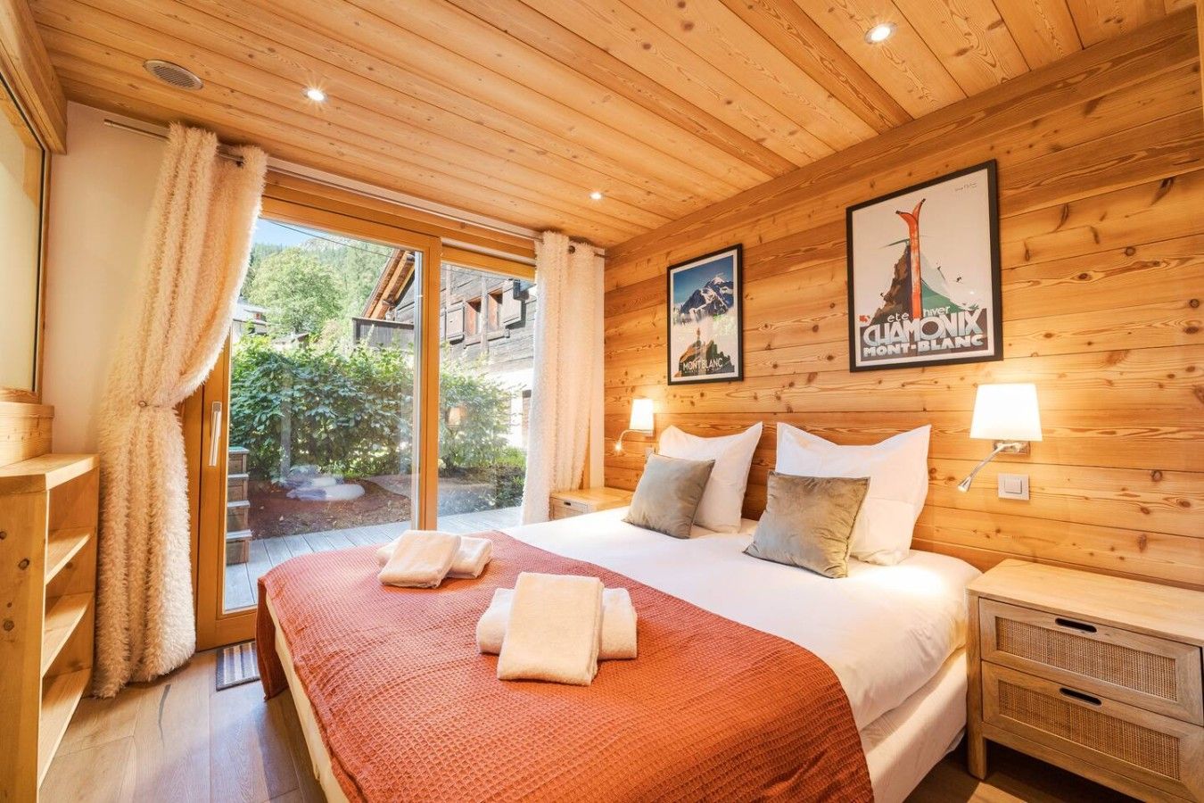 A hotel room with a large bed, wooden walls, a sliding glass door to an outdoor area, and two framed pictures on the wall.