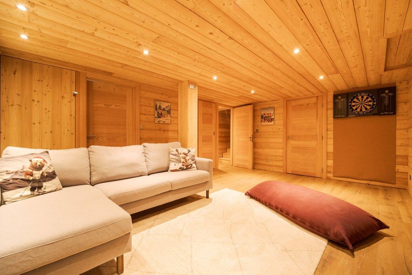 Quarto acolhedor com sofá, almofada vermelha, paredes de madeira e um alvo de dardos.