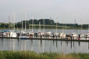A marina with multiple boats docked along a calm water body, surrounded by greenery. - Marina Hülsen - Skipper Lodge West (Kosel)