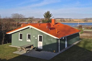 A green building with a red roof, a picnic table, and a view of a lake. - Marina Hülsen - Skipper Lodge West (Kosel)