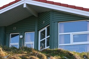 Un bâtiment écologique avec un toit rouge, des encadrements de fenêtres blancs et une fenêtre visible, ornée d’un rideau.