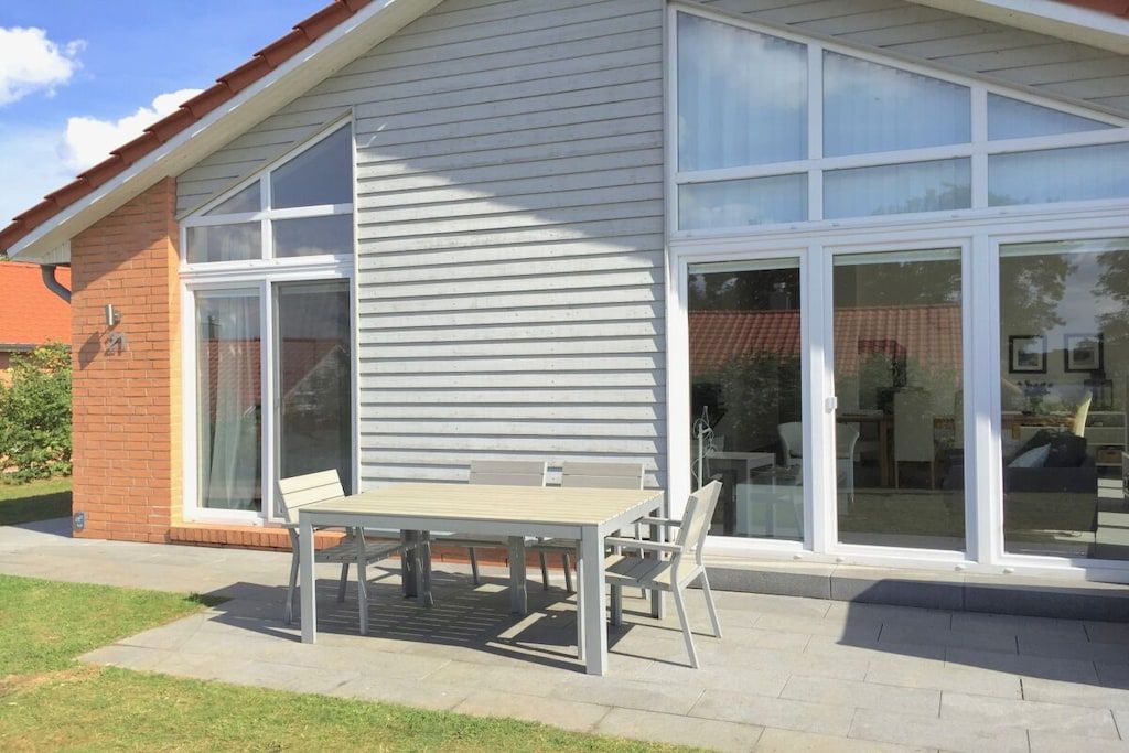 En bostadsbyggnad med en uteplats som har ett bord och stolar, stora skjutbara glasdörrar och en fasad av tegel.