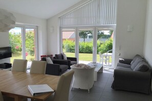 A modern living room with a dining table, sofas, and a large sliding glass door leading to a garden. - Holiday home in Kosel with swimming pool (Kosel)