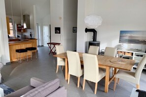 A modern kitchen with a central island, a dining area with a wooden table and chairs, and a living space with a sofa. - Holiday home in Kosel with swimming pool (Kosel)