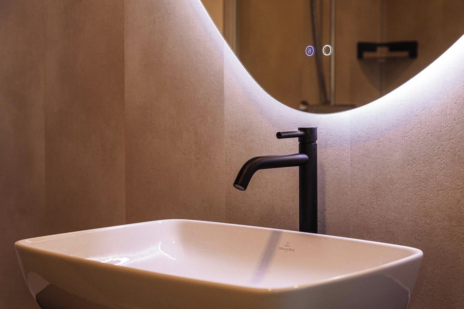A bathroom with a white rectangular sink, black faucet, and a curved mirror reflecting the wall and ceiling.