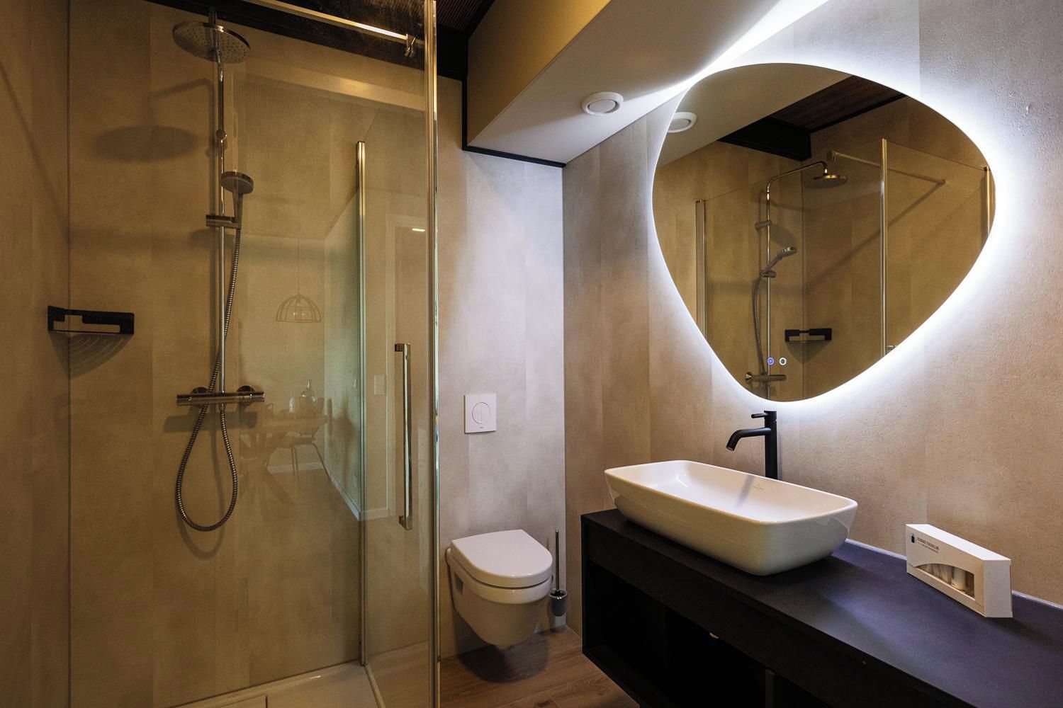 Un baño moderno con ducha envuelta en vidrio, inodoro y tocador con un espejo grande.