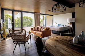 Une chambre d’hôtel moderne dotée d’un grand lit, d’un canapé, d’une table à manger et d’un balcon offrant une vue sur les arbres.