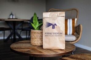 A paper bag with a logo and text on a round wooden table, accompanied by a potted plant and wicker furniture. - Spacious and comfortable Studio for 2 persons (Midsland)