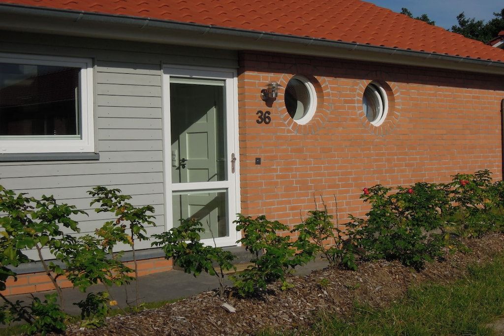 A house with a number 36 on the brick wall, a white door, and two circular windows.