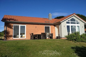 Ein zweistöckiges Haus mit Backsteinfassade, großen Fenstern und einer überdachten Terrasse.