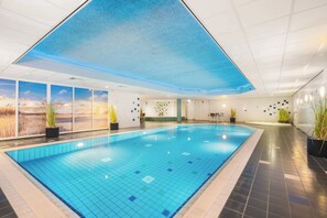 Ein Hallenbad mit Fliesenboden und -wänden, einer blauen Decke und Kübelpflanzen.