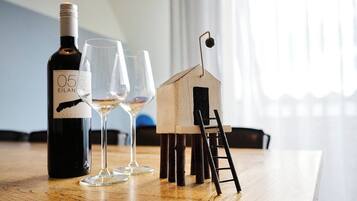 A bottle of wine, two glasses, and a small wooden house model on a wooden table.