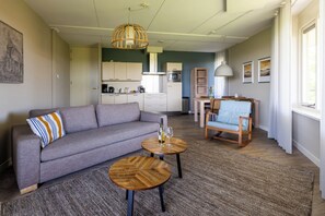 Una sala moderna con un sofá, dos mesitas de madera, un comedor con una silla y una cocina al fondo.