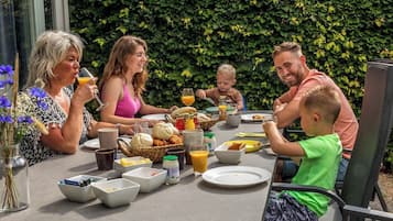 A family dining outdoors with a table set for breakfast, surrounded by greenery.