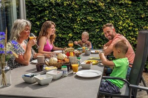 Una familia almorzando al aire libre, con una mesa lista para el desayuno, rodeada de follaje.