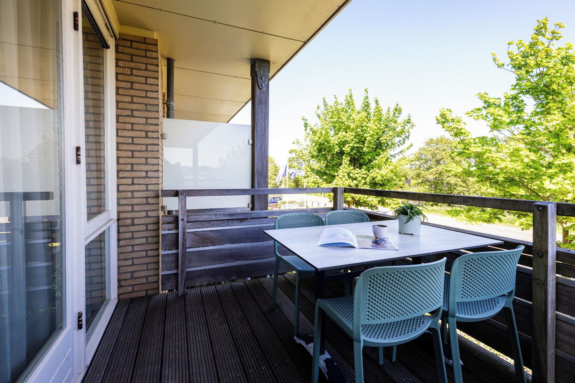 Ein Balkon mit Tisch und Stühlen, einer Topfpflanze und Blick auf Bäume.