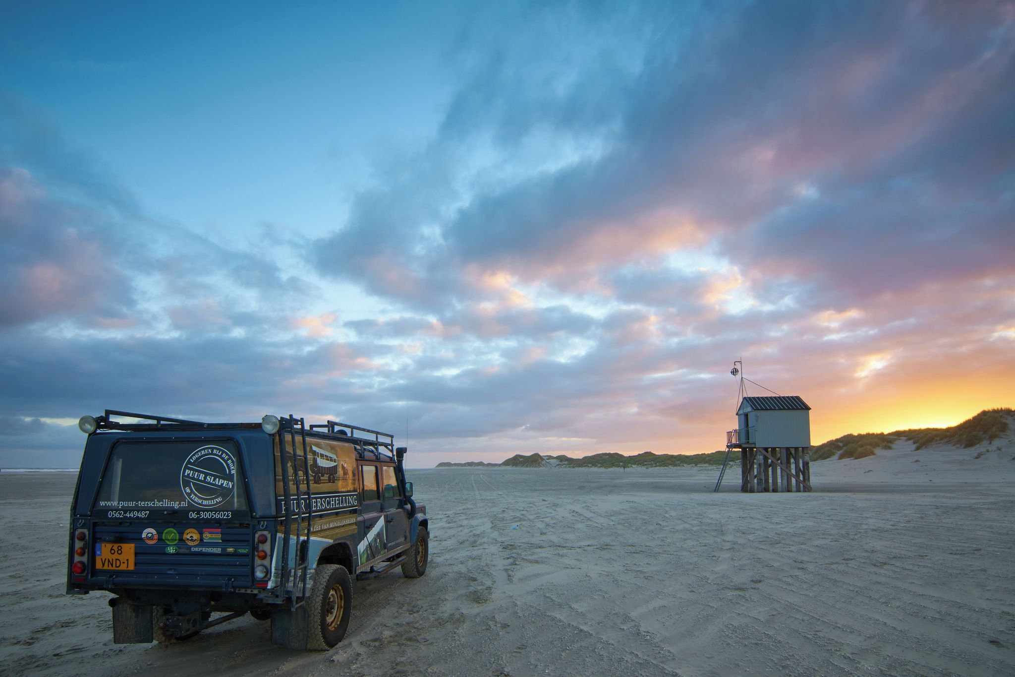 Un véhicule tout-terrain est garé sur une plage de sable, avec une tour de surveillance des sauveteurs en arrière-plan.