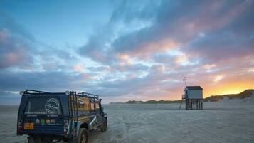 A dune buggy parked on a sandy beach with a lifeguard tower in the background.
