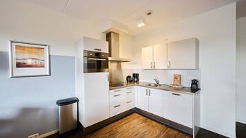 A modern kitchen with white cabinets, stainless steel appliances, and a wooden floor.