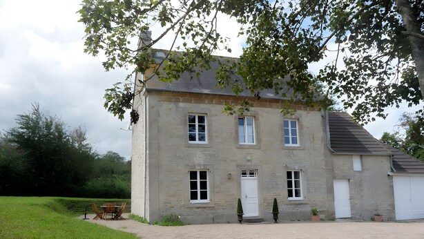 Ein zweistöckiges Steinhaus mit Kiesweg und Bank.