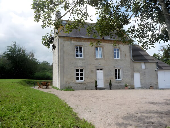 Un bâtiment en pierre de deux étages, avec une allée gravillonnée et un banc.