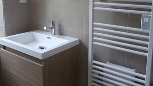 Ein modernes Badezimmer mit einem weißen Waschbecken, einem Spiegel und einem integrierten Handtuchhalter.