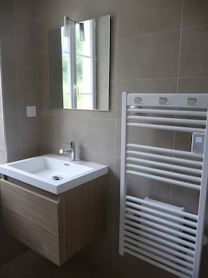 Une salle de bain moderne avec un lavabo blanc, un miroir et un porte-serviettes intégré.