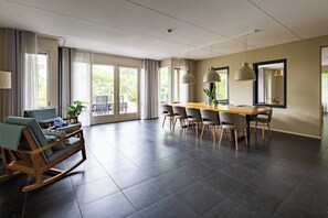 A spacious room with a dining table, chairs, a rocking chair, and large windows. - This spacious and luxurious apartment gives you a lot of comfort during your unforgettable stay on Terschelling. (Midsland)